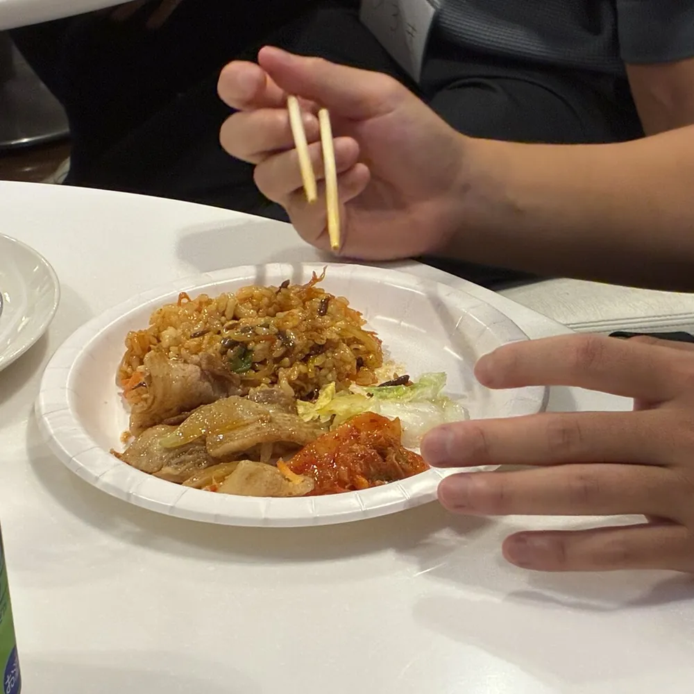 紙皿に取り分けた韓国料理と、お箸を持つ手元